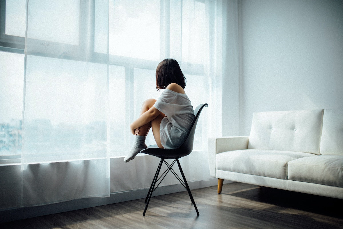 Frau die depressiv ist sitzt auf einem Stuhl und guckt aus dem Fenster raus
