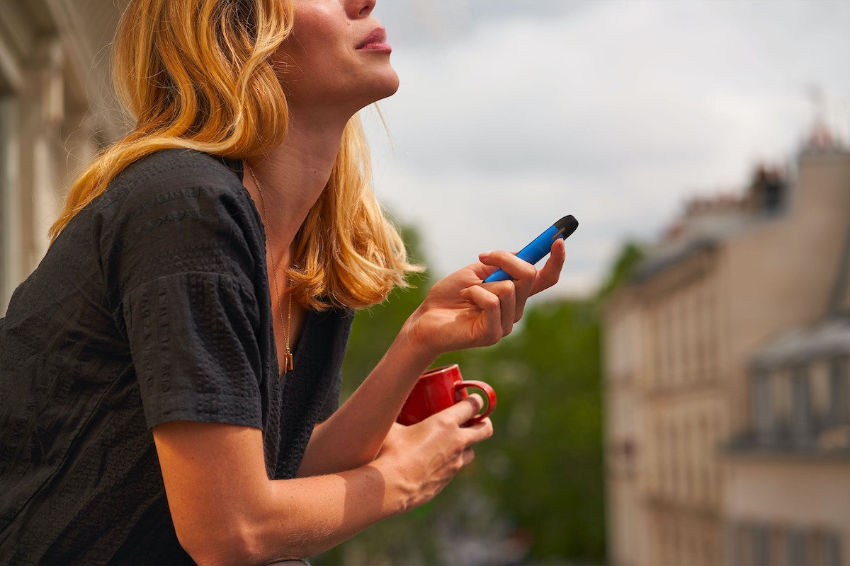 Eine Frau auf dem Balkon die ein THCP Vape Pen raucht und eine Kaffee Tasse hält