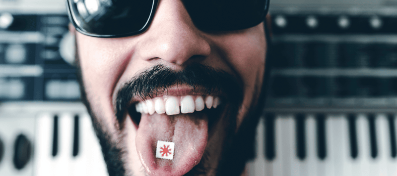 Mann hat ein 1D LSD Blotter im Mund mit einem Piano im Hintergrund